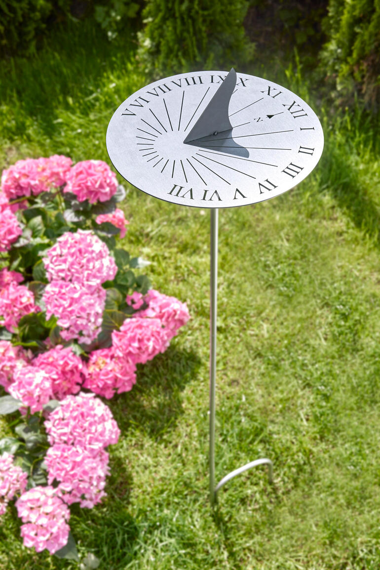 Edelstahl Sonnenuhr auf einem grünen Rasen, umgeben von pinken Blumen.