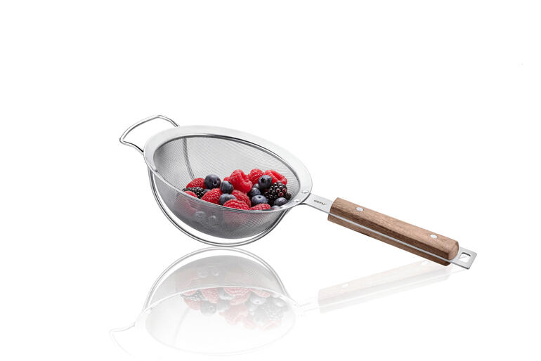 2 Bügel an der Sieb-Unterseite sorgen für festen Stand und Abstand zur Arbeitsfläche. Küchensieb mit roten Beeren darauf, auf einem weißen Hintergrund.