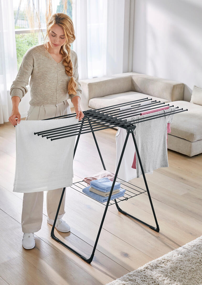 Frau organisiert Wäsche auf einem Design-Wäscheständer im Wohnraum