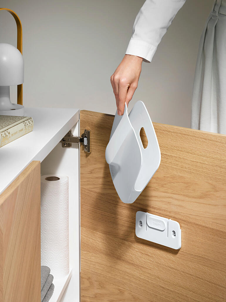 Nach Gebrauch eventuell noch anhaftende Krümel oder Staub sammeln sich im abnehmbaren Halter und können sauber entsorgt werden. Hand mit einer Kehrschaufel aus einem Schrank für eine praktische Aufbewahrung.