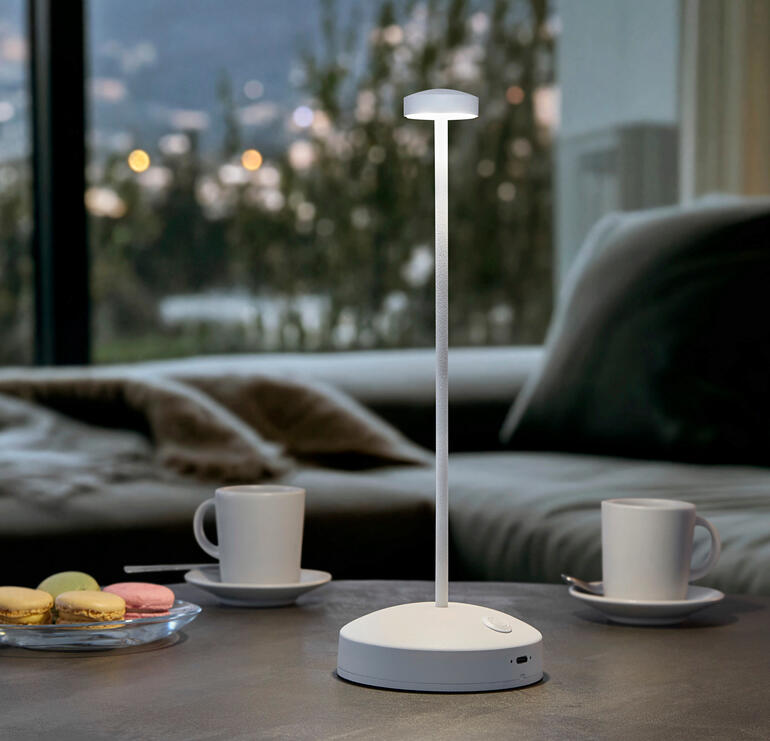 Weiß Design-Tischleuchte mit Akku, Farbe: Weiß, auf einem Tisch mit Getränken.