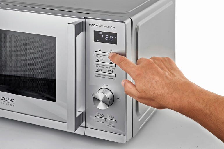 Hand drückt auf das Bedienfeld einer 3-in-1-Mikrowelle.