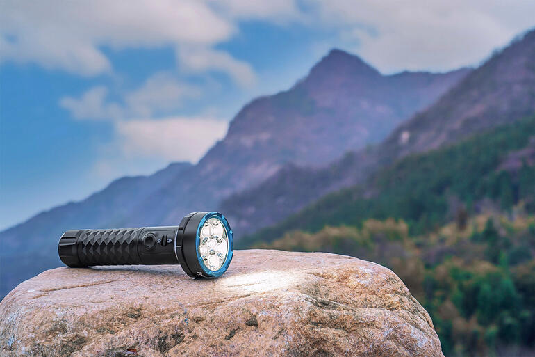 Bidirektionale 5.000 Lumen Taschenlampe auf einem Stein mit Berglandschaft im Hintergrund.