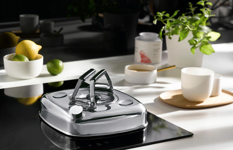 Design-Wasserkessel aus Edelstahl auf einem modernen Kochfeld mit frischen Zutaten.