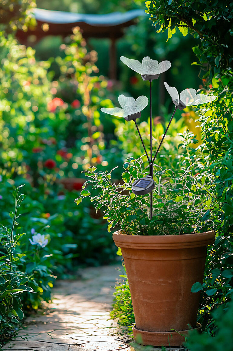 Auch tagsüber sind die nahezu transparenten Acryl-Schmetterlinge ein zauberhafter, filigraner Blickfang. Gartenstecker mit LED-Schmetterlingen in blühendem Garten.