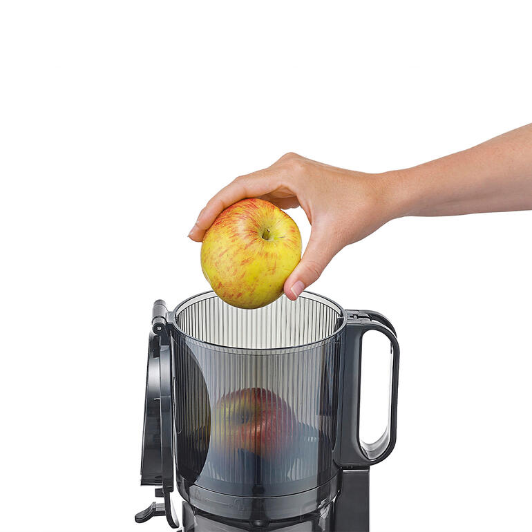 Mit 13 cm Ø großer XXL-Einfüllöffnung – perfekt für ganze Früchte. Hand, die einen Apfel in das obere Fach des CASO Slow-Juicers legt
