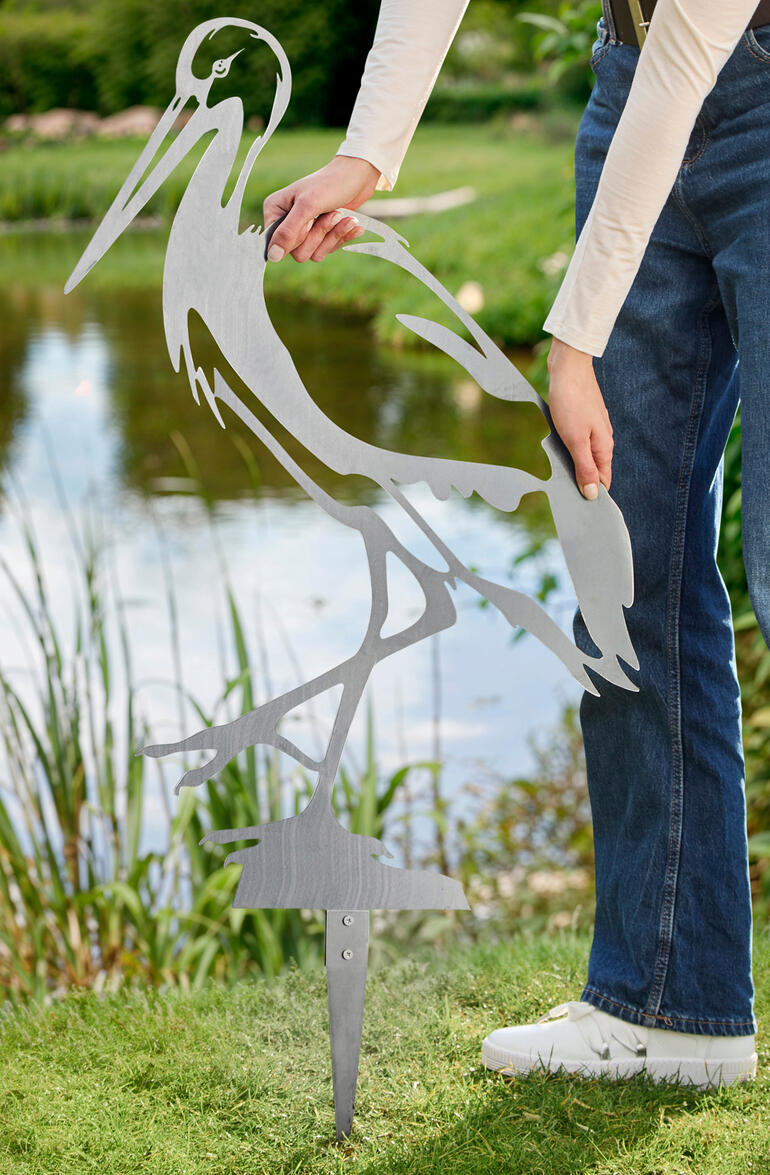 Person, die einen Gartenstecker in Form eines Storches in den Boden steckt