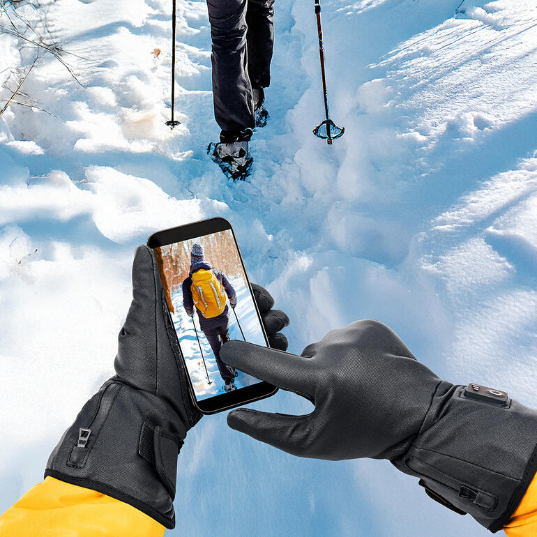 Stets warme Hände und dennoch können Sie jederzeit das Smartphone bedienen. Hand mit Smartphone, die den Benutzer im verschneiten Gelände zeigt.