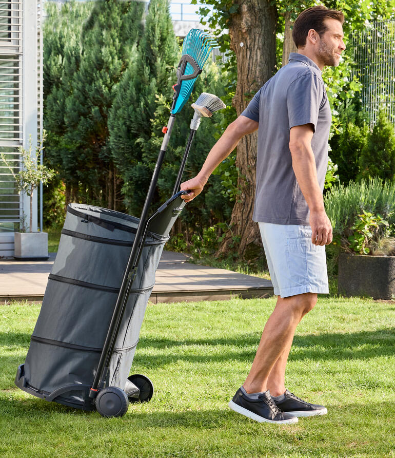 Mann zieht einen faltbaren Gartentrolley mit Laub durch den Garten.