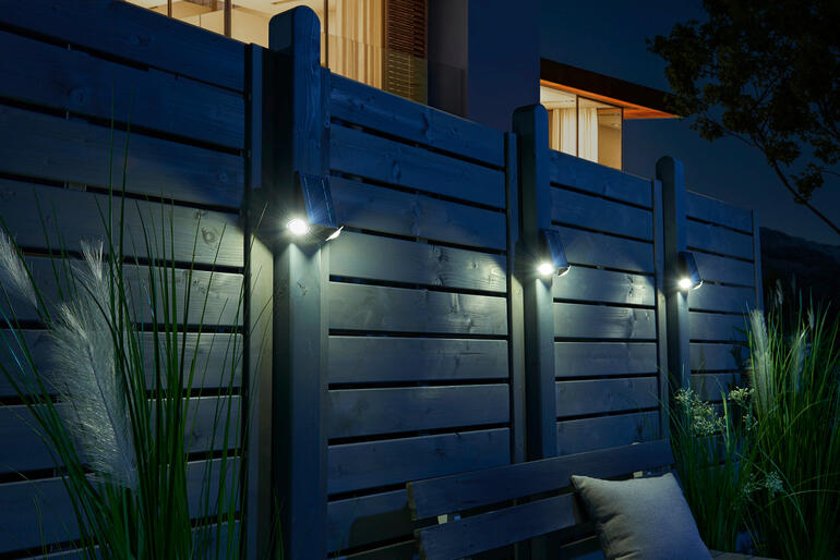 Intelligenter Solarstrahler beleuchtet eine Holzhecke bei Nacht.