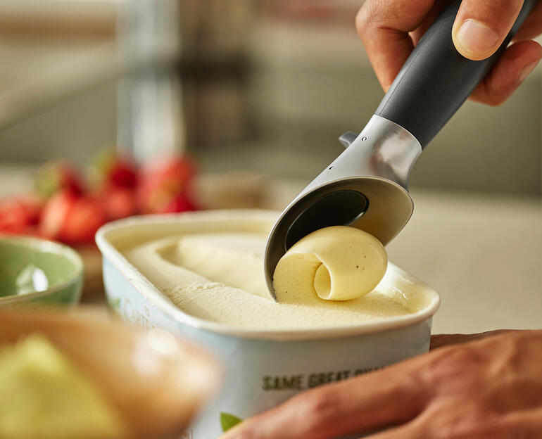 Hand, die Eis mit einem Portionierer aus einem Behälter mit Eiscreme entnimmt.