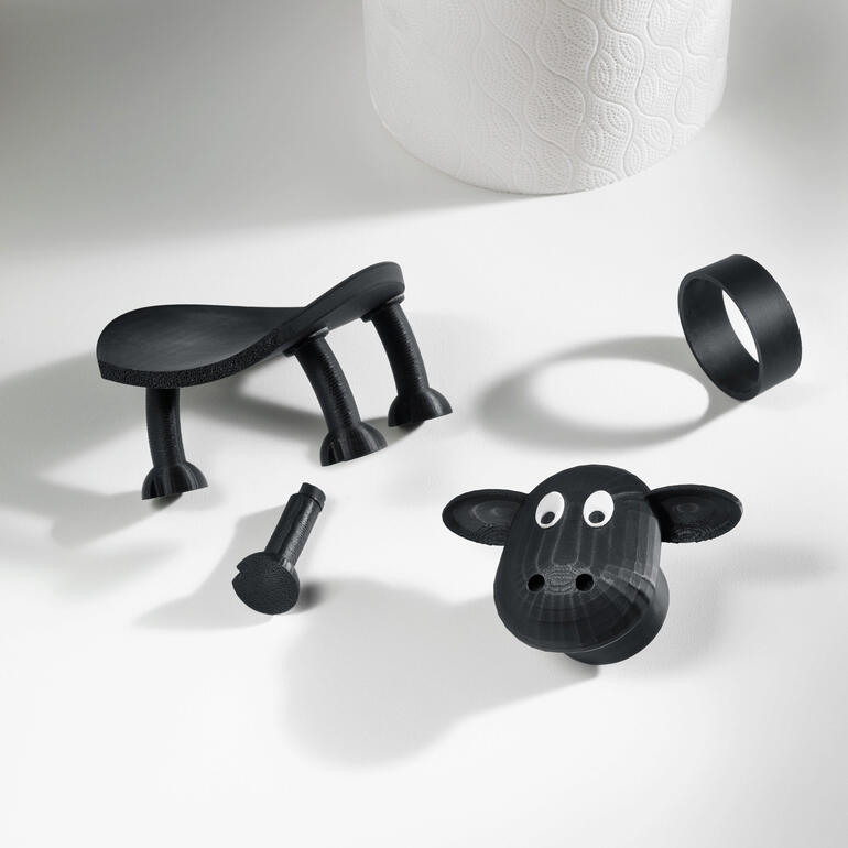 Komplett im 3D-Druckverfahren in Deutschland hergestellt. Zerteilte Teile eines Toilettenpapierhalters in Schaf-Design auf einem Tisch.