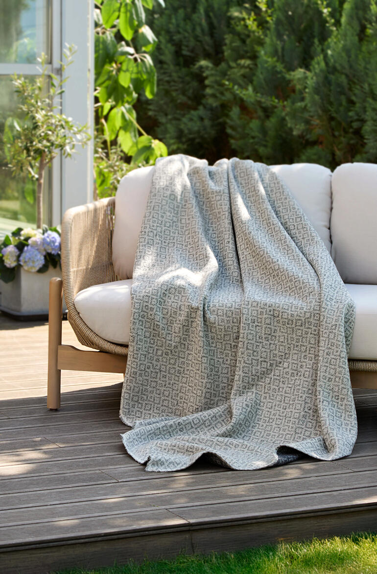 Umkehrbare jacquard Decke liegt auf einer Gartenbank.
