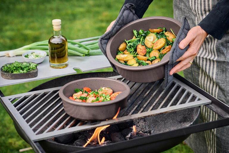 Keltentopf mit Gemüse wird vom Grill genommen.