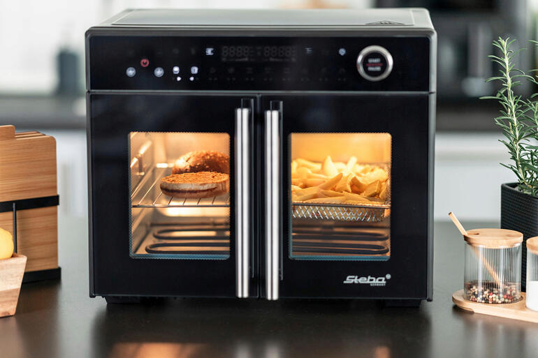 Airfry-Grillbackofen Tri-Zone mit offenen Türen und sichtbar zubereiteten Pommes.