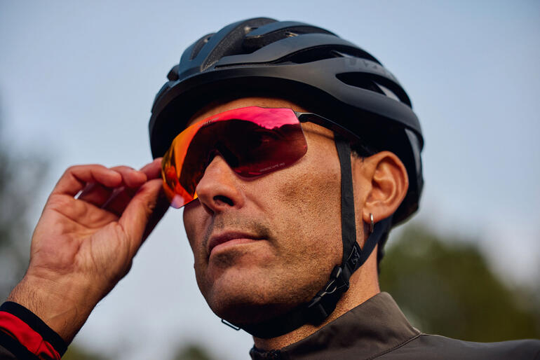 Mann mit roter Sport-Sonnenbrille und schwarzem Helm, der die Brille anpasst.