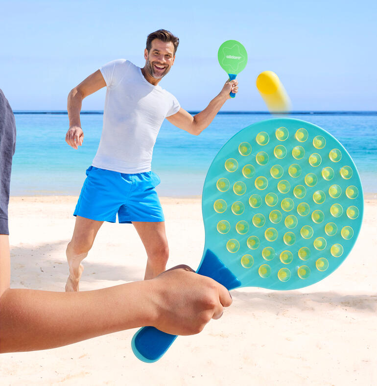 Mann spielt am Strand mit einem ovalen Schlagspiel und trifft den Ball.