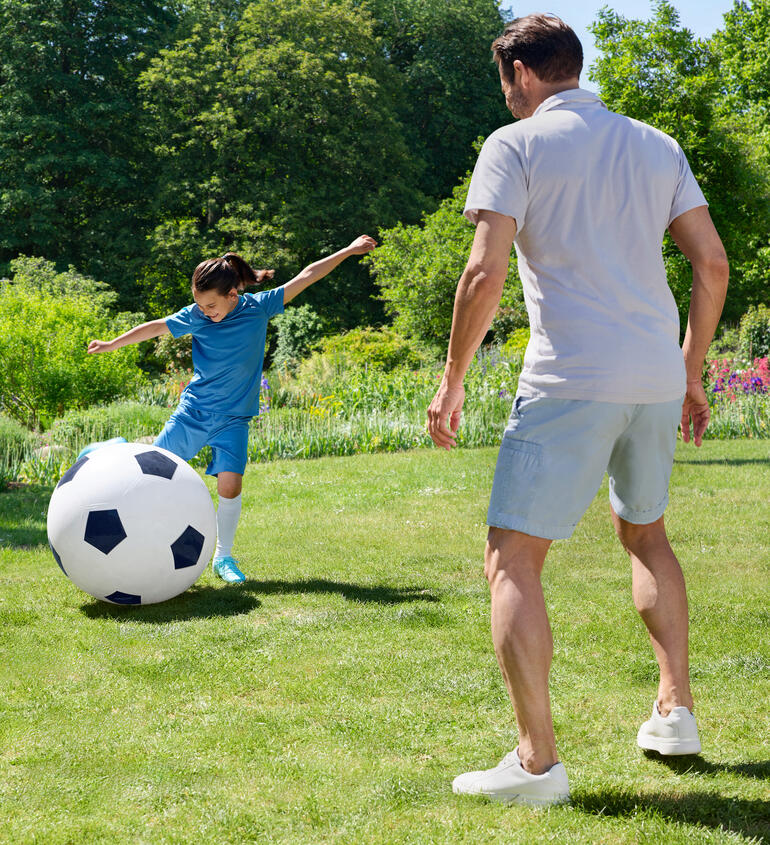 Ein Junge spielt mit einem übergroßen Fußball im Garten.