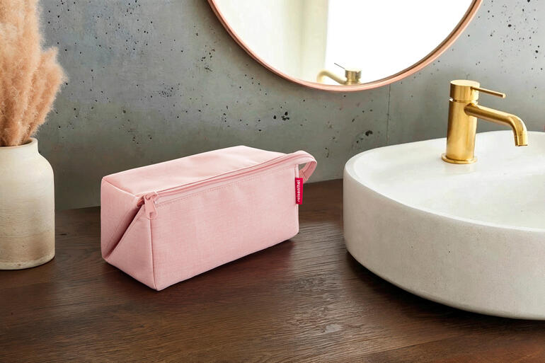 Rosa 2-in-1 Reisenecessaire auf einem Holztisch neben einem Waschbecken