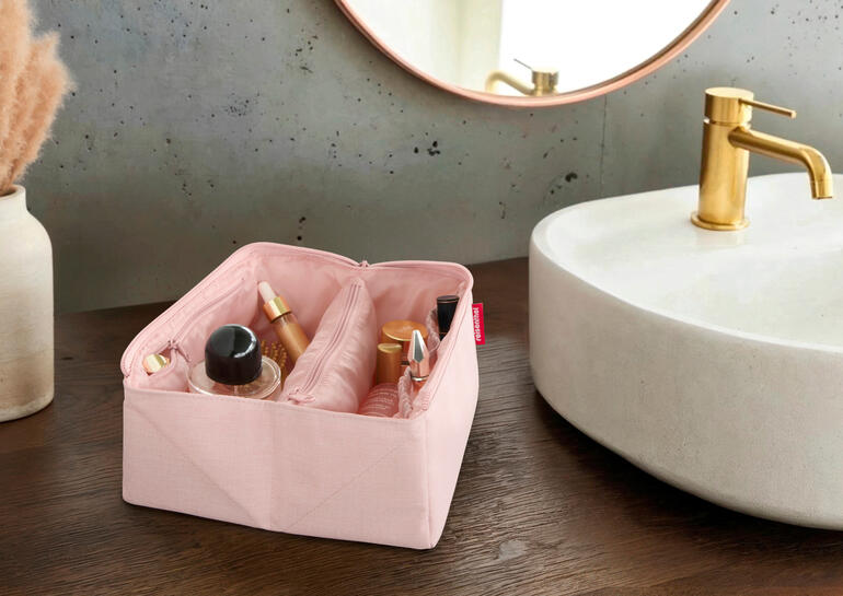 Offenes rosa 2-in-1 Reisenecessaire mit Pflegeprodukten auf einem Holztisch