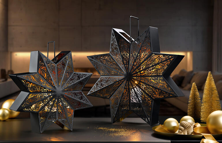 Zwei dekorative Windlichter in Sternform auf einem Tisch mit goldenen Weihnachtskugeln.