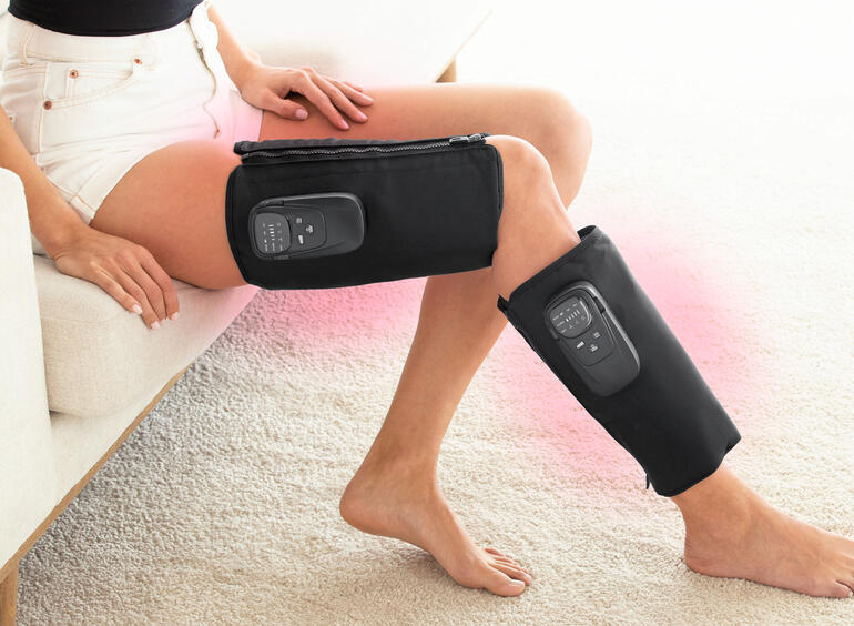 Frau mit einem Kompressions-Massagegerät an den Beinen, während sie sitzt.