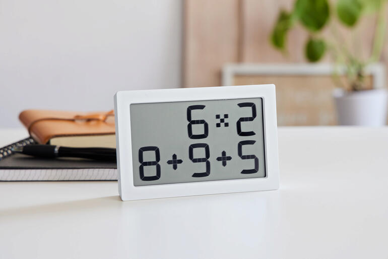 Tischuhr mit digitaler Anzeige für mathematische Aufgaben in Weiß.