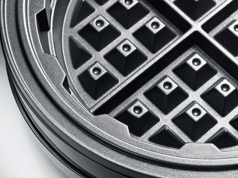 Die umlaufende Rinne fängt überschüssigen Teig auf. Nahaufnahme des Waffeleisenrackets mit Waffelmuster.