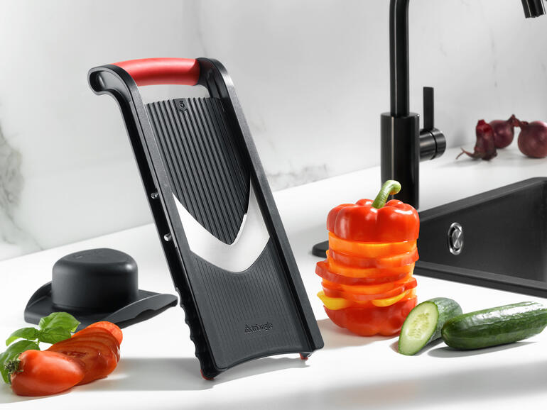 Gemüsehobel mit Restehalter, präsentiert neben frischem Gemüse.