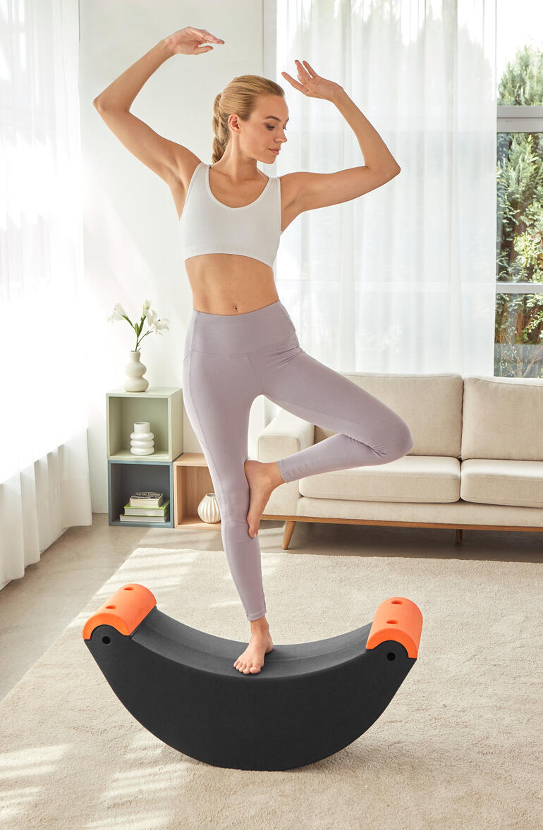 Ideal auch zur Intensivierung Ihrer Yoga-Asanas. Frau steht auf einem 3-in-1 Multifunktions-Trainer und balanciert auf einem Bein.