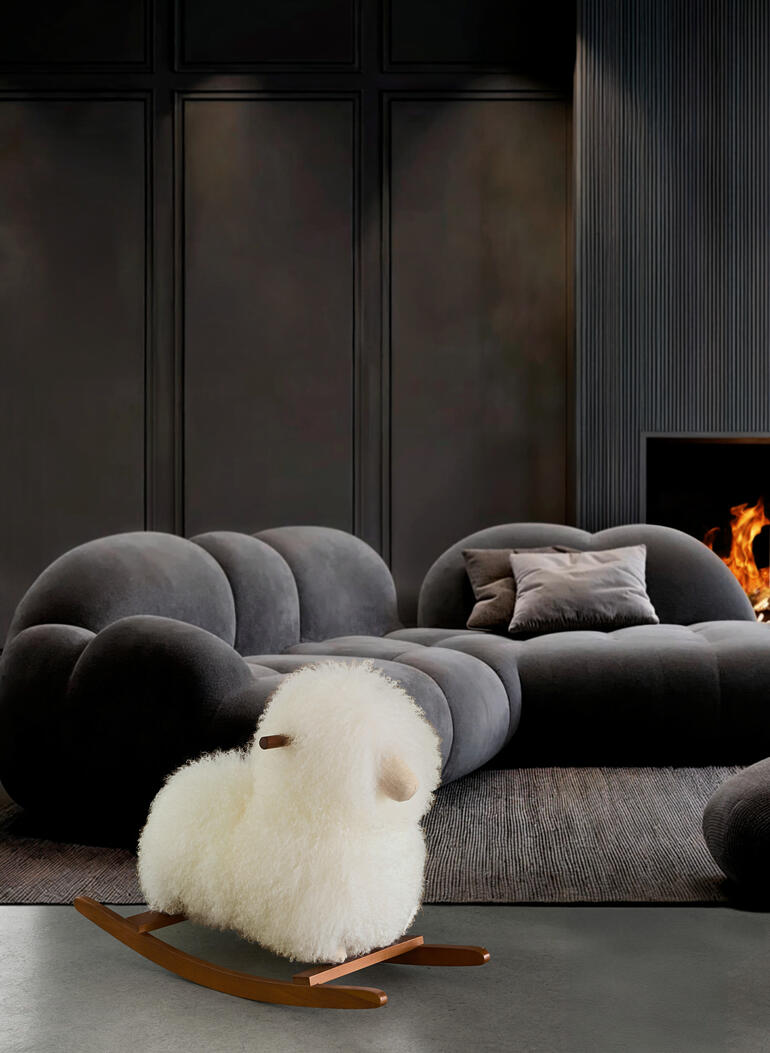Ein stilvolles Designobjekt für Erwachsene – und ein kuschelweiches Reittier für Kinder. Schaukelschaf aus echtem Fell vor einem modernen Sofa.