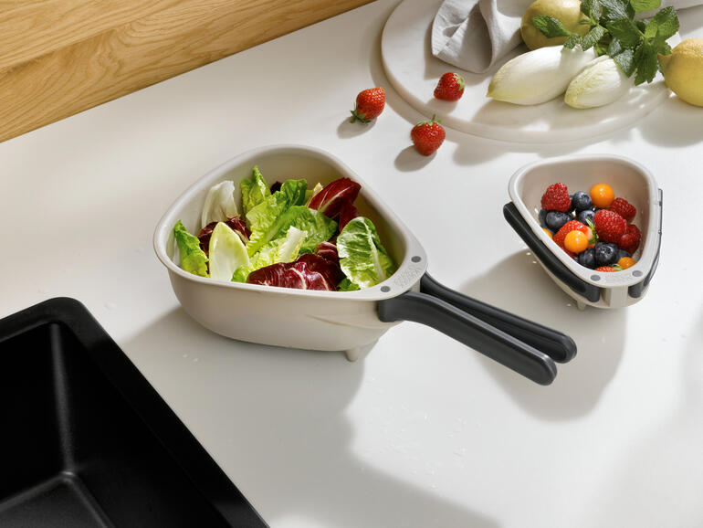 Platzsparendes Küchensieb mit frischem Gemüse und Obst im Hintergrund.