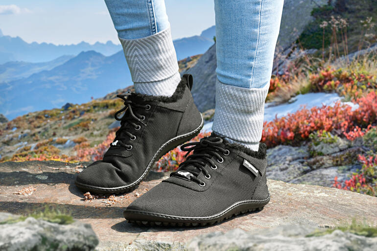 Frau trägt schwarze Winter-Sneaker auf einer felsigen Unterlage in den Bergen.