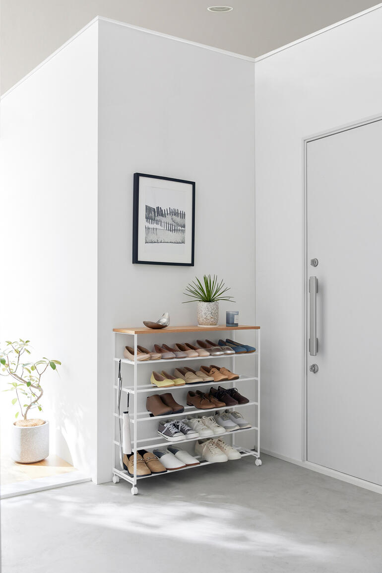 Rollbares Schuhregal in Schwarz mit mehreren Fächern für Schuhe, auf einem grauen Boden.