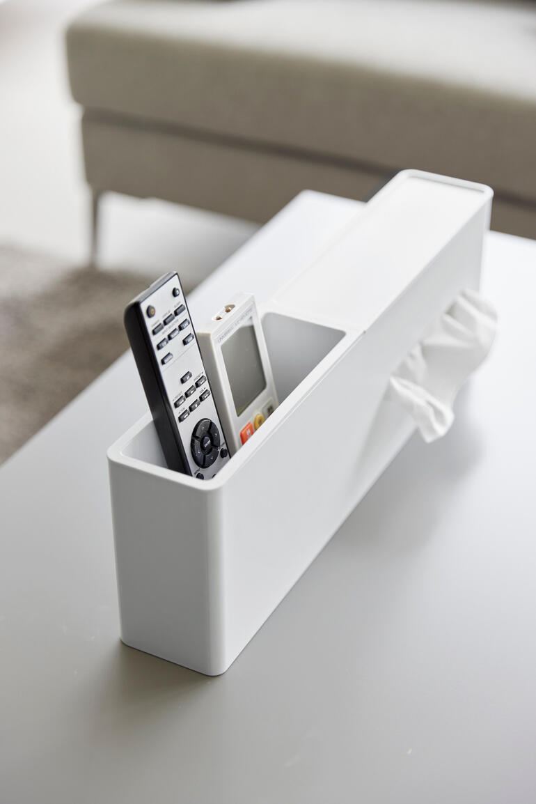 Weiße Taschentuchbox mit Fernbedienung und Smartphone auf einem Tisch.
