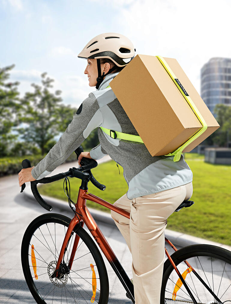 Mann auf Fahrrad mit Paketrucksack, der ein großes Paket transportiert.