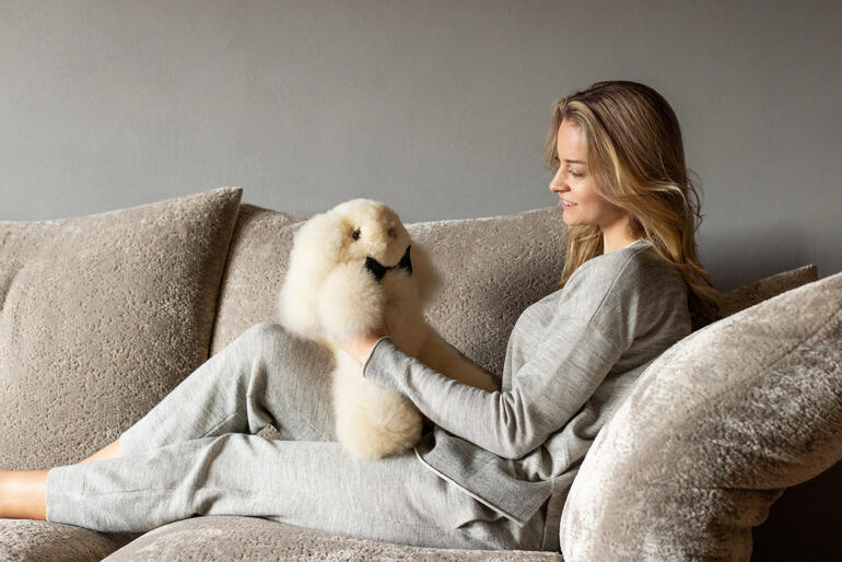 Frau spielt mit einem kleinen, champagnerfarbenen Alpaka-Hasen auf einer Couch.
