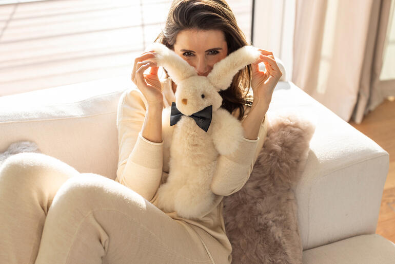Frau posiert mit einem kleinen Champagnerfarbigen Alpaka-Hase auf einem Sofa.