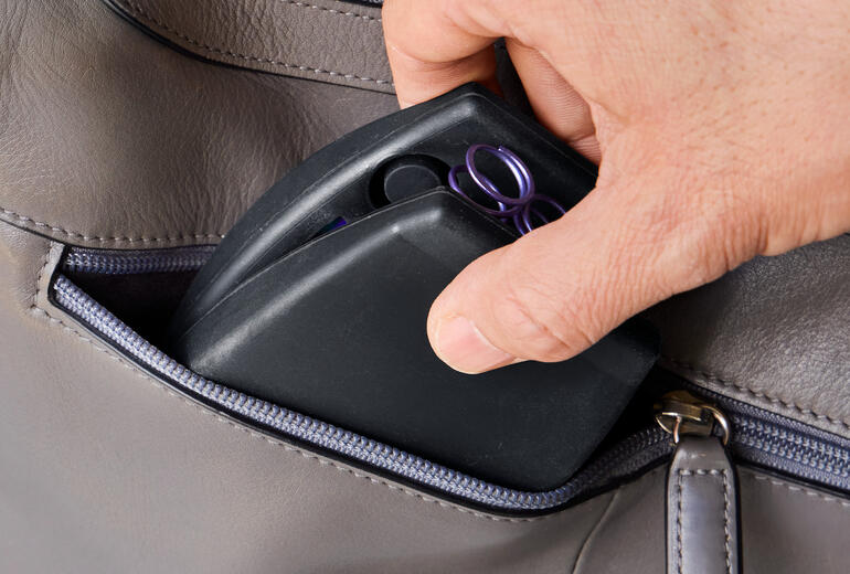 Ideal zum Mitnehmen – z. B. für das Training im Park und auf Reisen. Hand greift Kompakt-Oberkörpertrainer aus einer Tasche