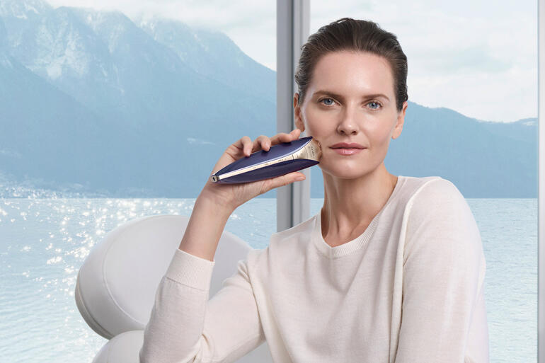 Frau hält ein Anti-Aging-Gerät im Freien, mit Bergen im Hintergrund.