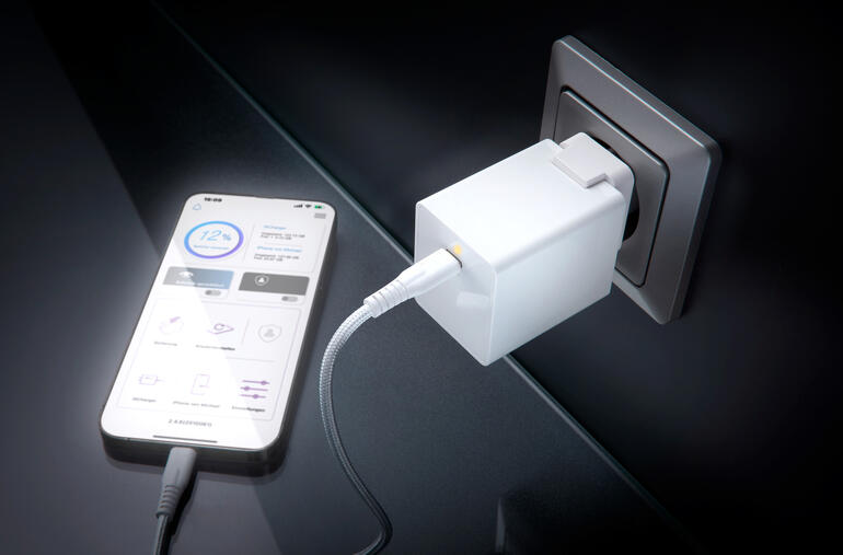 Weißer USB-Ladeadapter steckbar in eine Wandsteckdose, Smartphone angeschlossen.