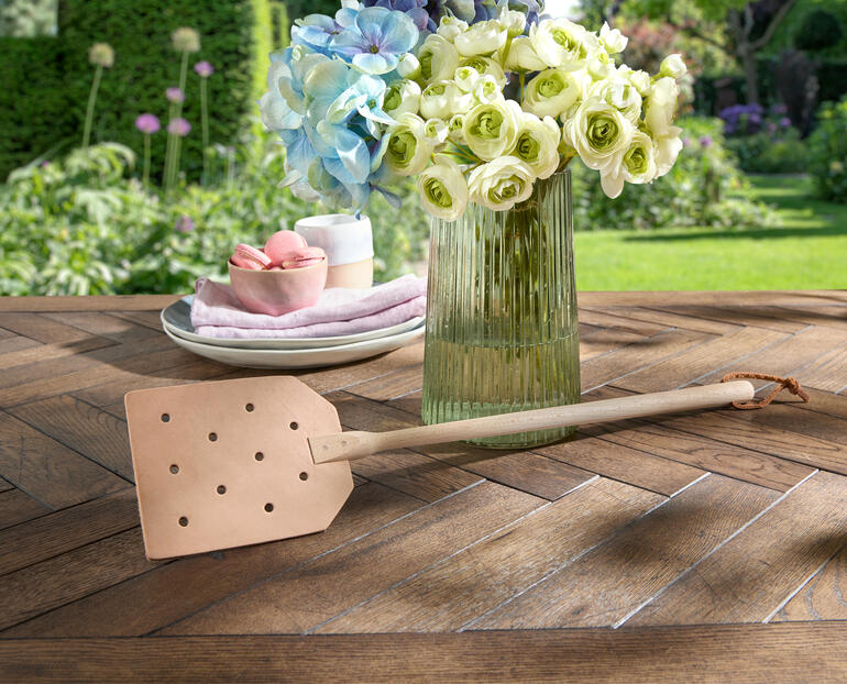 Leder-Fliegenklatsche liegt dekorativ auf einem rustikalen Holztisch.