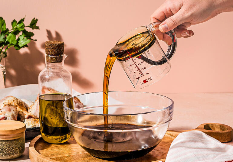 Person gießt Öl aus einem Messbecher in eine Schüssel.