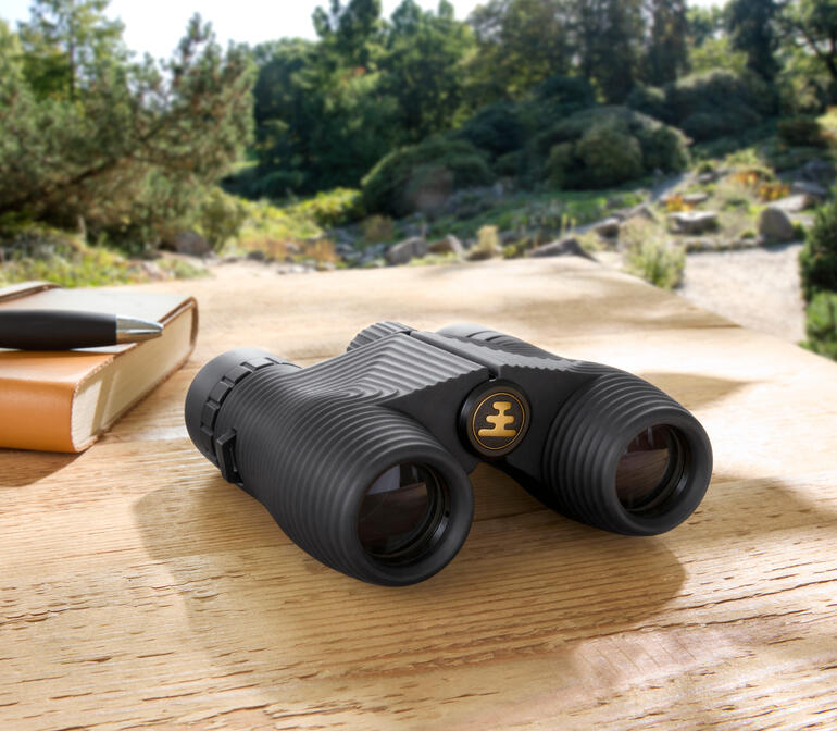 Kompakt-Fernglas auf einem Holztisch in der Natur.