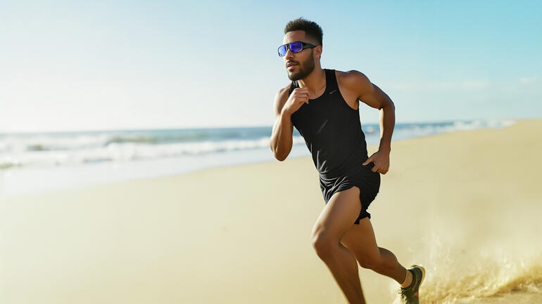Mann in Sportkleidung läuft am Strand mit Lichtbrille.