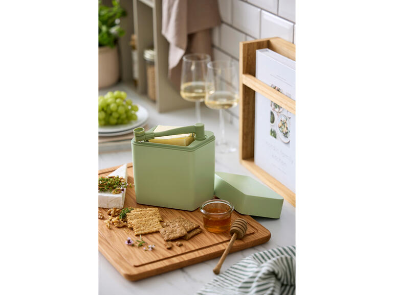 Käse Frischebox mit Schneider auf einem Holzbrett neben Crackern und Honig.