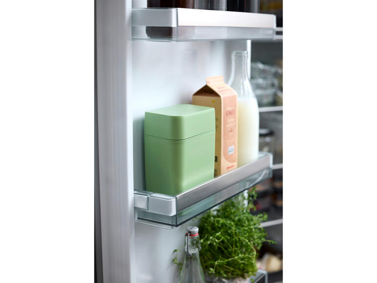 Käse Frischebox im Kühlschrank, umgeben von Milch und Kräutern.