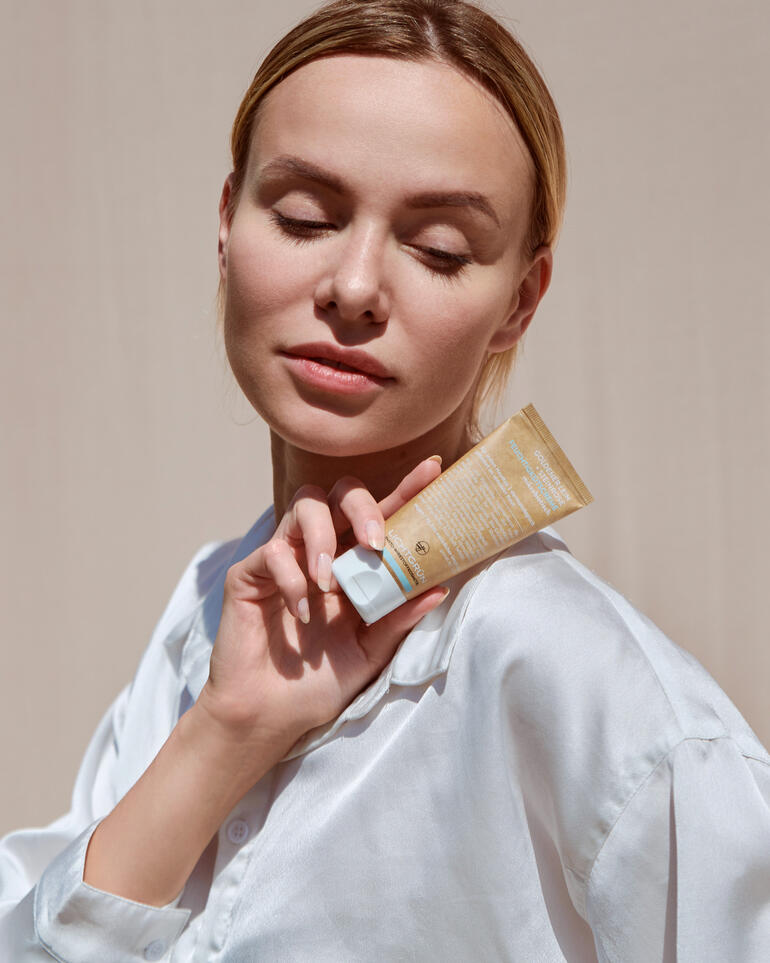 Frau mit geschlossenen Augen hält eine Tube Naturkosmetik in der Hand.