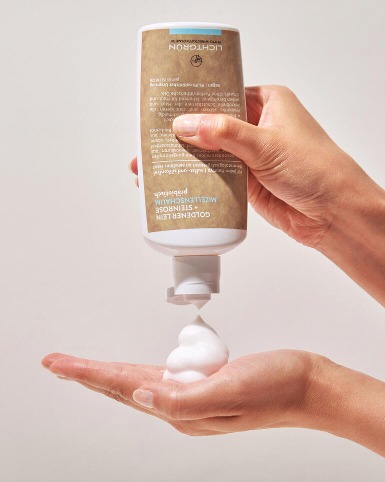 Hand hält eine Dose Naturkosmetik mit schäumender Textur, während die andere Hand etwas Schaum aufnimmt.