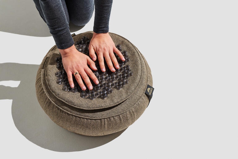 Frau drückt auf das Shakti-Meditationskissen mit beiden Händen.